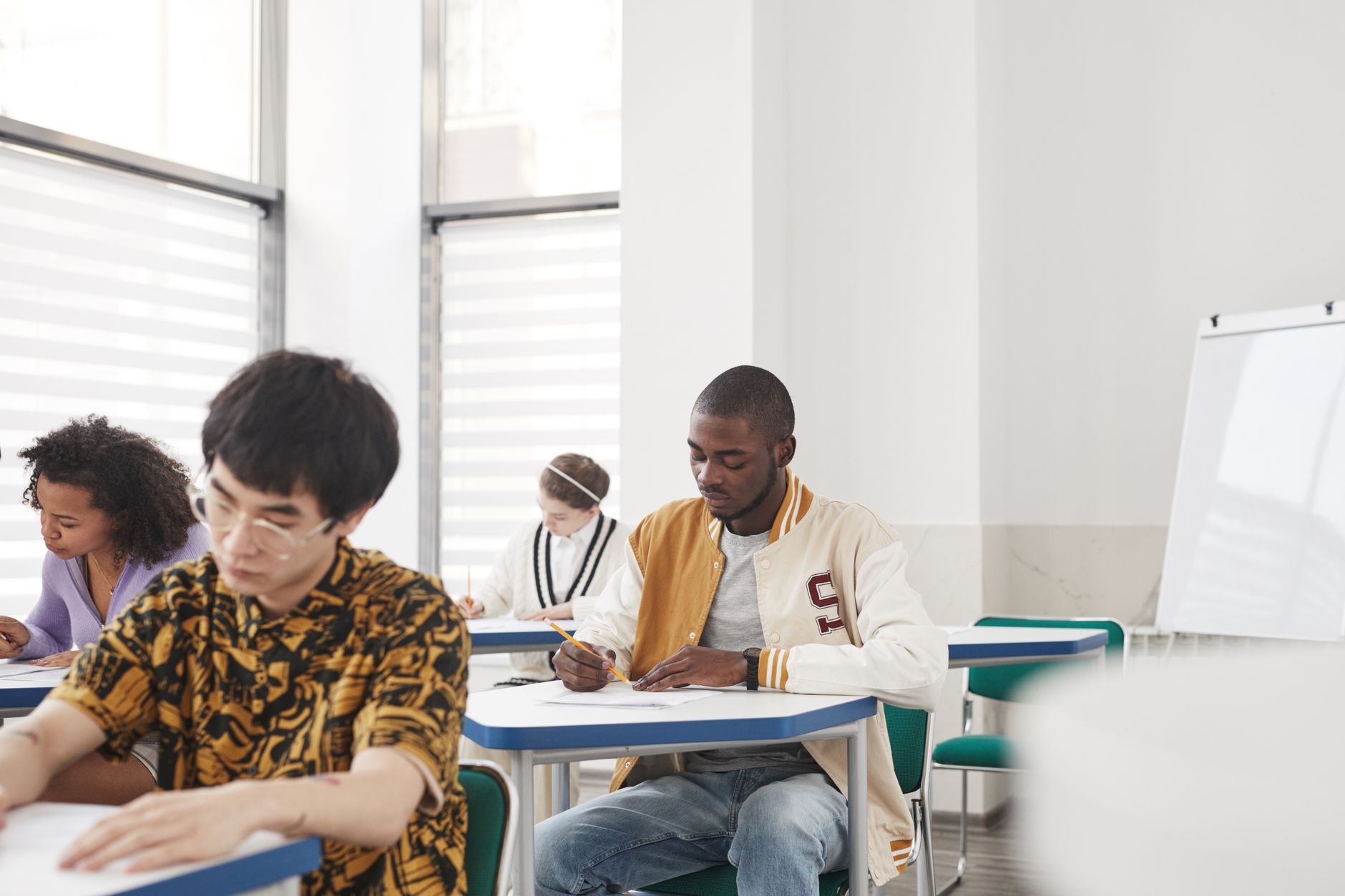 Students seated at desks in a large exam hall taking a standardized test.