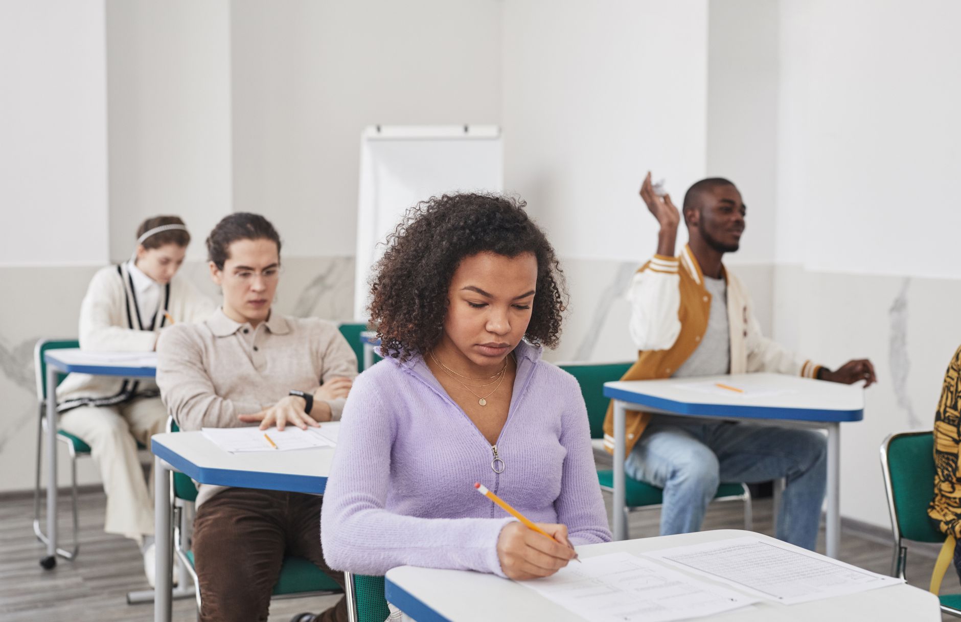 Students sitting at desks in a testing hall, focused on writing their exam booklets.